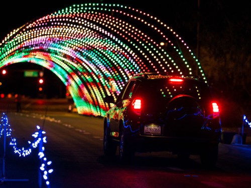 A car drives through a colorful, illuminated light tunnel on a dark road.