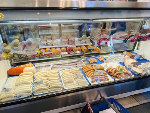 A display case filled with various types of sausages and deli meats, neatly arranged on trays.