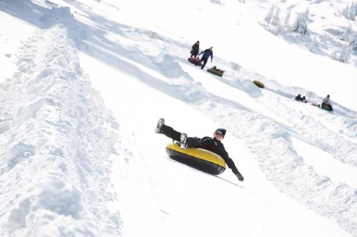 A person in a black jacket enjoys tubing down a snowy slope, with others in the background on similar tubes.
