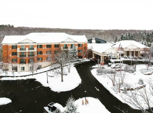 A snowy landscape featuring a brick hotel and surrounding trees, with a clear sky above.