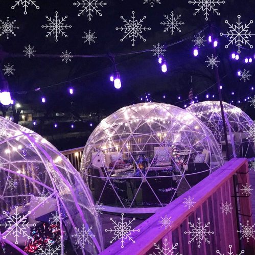 Cozy igloos adorned with string lights, surrounded by snowflakes, create a festive winter atmosphere at night.