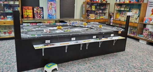 A model racetrack with toy cars, surrounded by colorful displays of vintage toys in a museum-like setting.