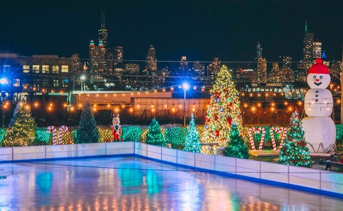A festive ice skating rink surrounded by Christmas trees, lights, and decorations, with a city skyline in the background.