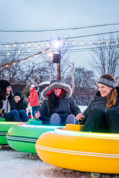 A group of friends enjoying a winter activity on colorful inflatable tubes, surrounded by festive lights and snow.