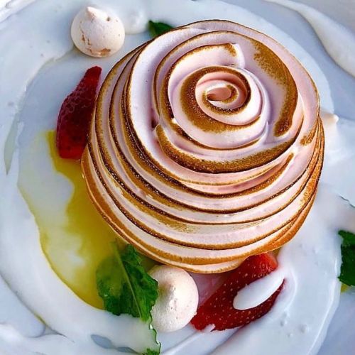 A beautifully crafted dessert resembling a rose, with swirls of pink and gold, surrounded by strawberries and cream.