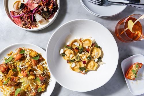 A table setting with three dishes: pasta, a salad, and a baked dish, alongside a drink with a lemon garnish.