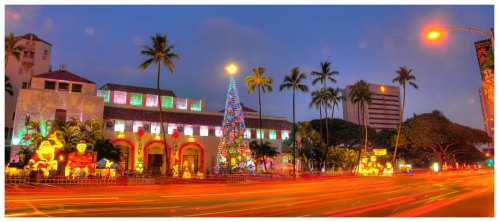 A festive scene featuring a brightly lit Christmas tree, decorations, and palm trees at dusk, with traffic lights glowing.