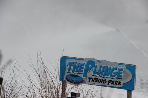 Sign for "The Plunge Tubing Park" with misty background, suggesting a winter tubing attraction.