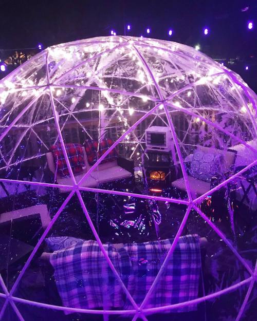 A cozy, illuminated dome with string lights, featuring seating and a small heater inside.