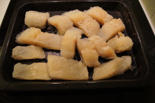 Pieces of translucent, gelatinous fish or seafood arranged on a black baking tray.