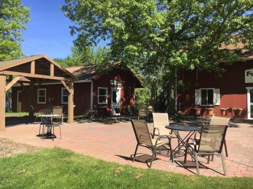 A sunny outdoor area with patio furniture, a wooden gazebo, and red buildings surrounded by green trees.