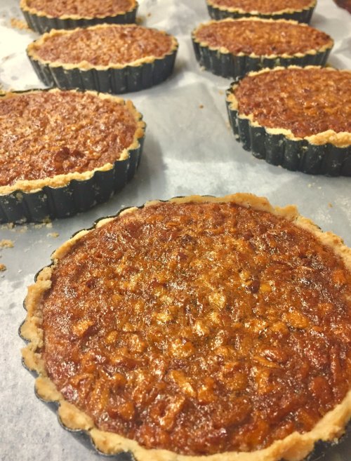 Freshly baked mini pecan pies in black tart pans, arranged on parchment paper.