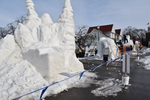 Snow sculptures in a winter festival, featuring tall, intricate designs and a snowy landscape with people working nearby.