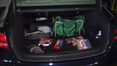 A car trunk filled with various items, including a green duffel bag, tools, and a first aid kit.