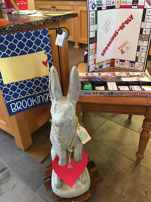 A stone rabbit statue with a heart, next to a Brookings-themed Monopoly game and a decorative sign.