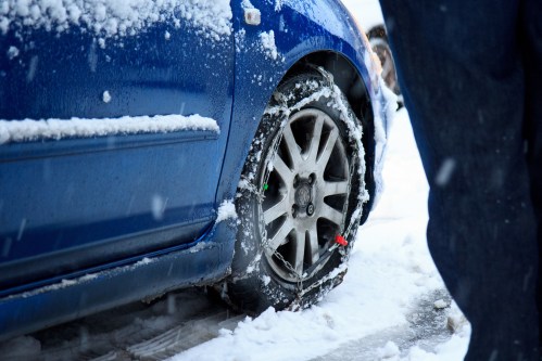 A blue car with a flat tire covered in snow, surrounded by a wintery landscape.