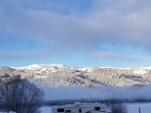 Snow-covered mountains under a blue sky, with fog in the valley and an RV in the foreground.