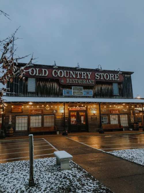 A rustic country store and restaurant with a snowy exterior, warmly lit under a gray sky.