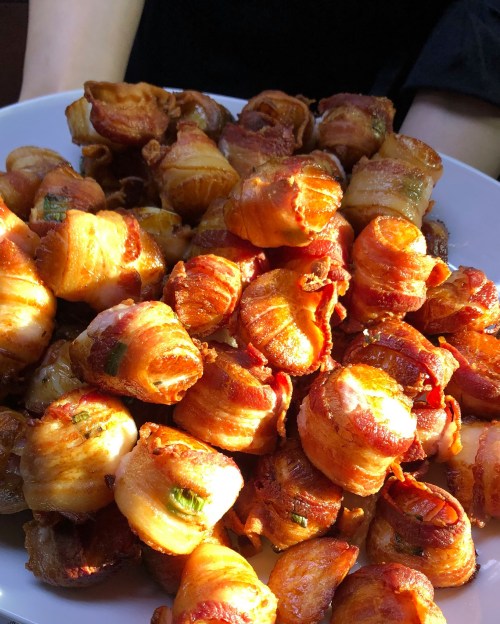 A close-up of a large plate filled with crispy, bacon-wrapped appetizers, golden brown and glistening.