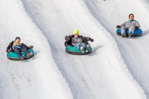 Three people are tubing down a snowy slope, enjoying a winter day.