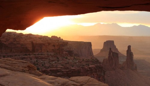Sunset over a rugged canyon landscape, with rock formations silhouetted against a colorful sky.