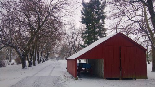 A red barn beside a snowy road, surrounded by bare trees and a winter landscape.
