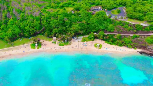 Aerial view of a tropical beach with turquoise water, sandy shore, and lush green surroundings.