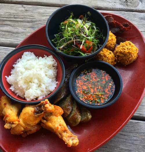 A vibrant plate featuring chicken wings, rice, salad, dipping sauce, and corn fritters on a rustic wooden table.