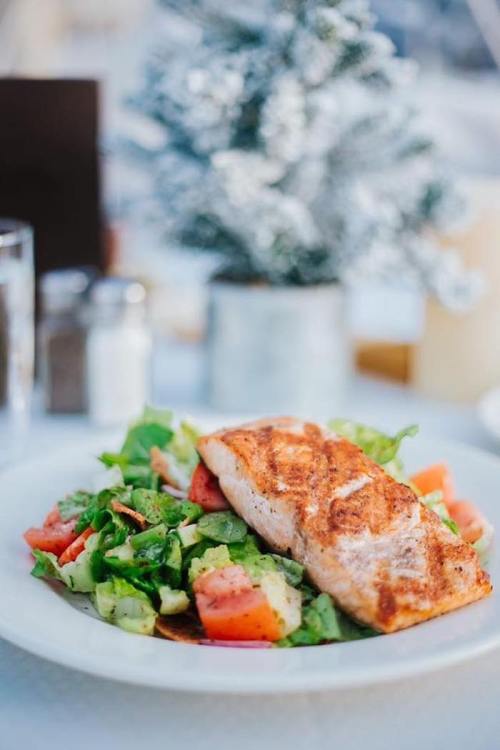 A plate of grilled salmon served with a fresh salad of greens, tomatoes, and cucumbers, with a festive tree in the background.