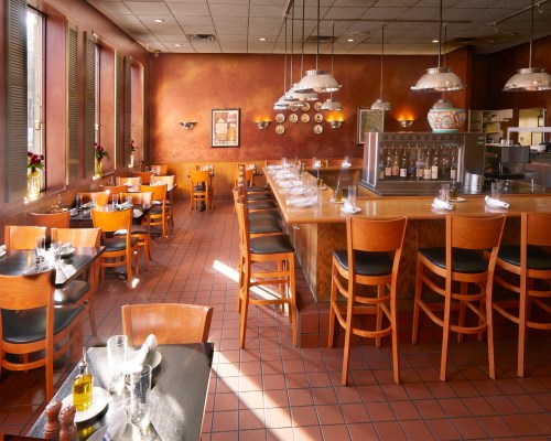 A warm, inviting restaurant interior with wooden chairs, tables set for dining, and soft lighting.