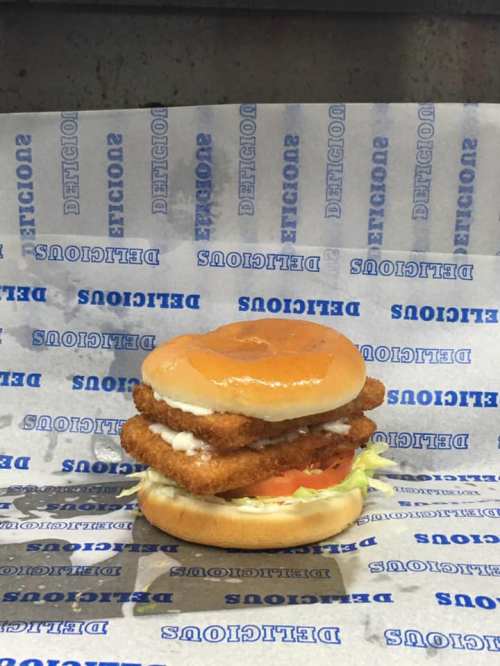 A stacked chicken sandwich with lettuce, tomato, and sauce on a bun, placed on blue and white patterned paper.