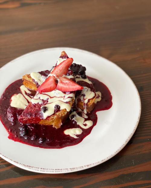 A slice of dessert topped with strawberries and drizzled with cream, served on a plate with berry sauce.