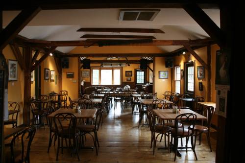 Cozy restaurant interior with wooden tables and chairs, warm yellow walls, and large windows letting in natural light.
