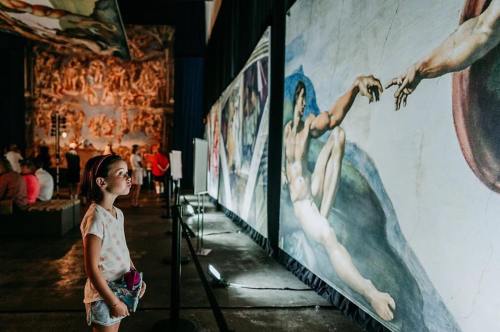A child gazes at a large mural of Michelangelo's artwork in an art exhibition.