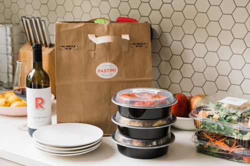 A takeout bag from Pastini with wine, plates, and containers of food on a kitchen counter.