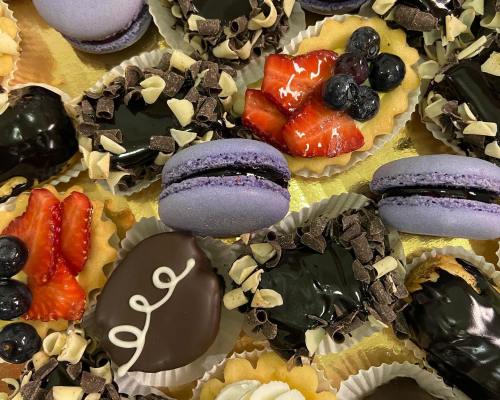 A colorful assortment of desserts, including macarons, fruit tarts, and chocolate-covered treats, arranged on a platter.