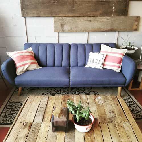 A blue sofa with striped pillows sits in a cozy room, next to a wooden coffee table and potted plants.