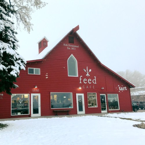 A red barn-style café with snow on the ground, featuring large windows and a sign that reads "feed café."