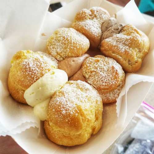 A basket of cream puffs dusted with powdered sugar, filled with various creamy fillings.