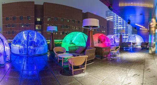 Colorful illuminated igloos on a rooftop terrace, surrounded by modern furniture and a city skyline at night.
