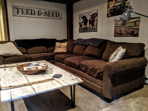 Cozy living room with a brown sectional sofa, rustic coffee table, and farm-themed wall art.