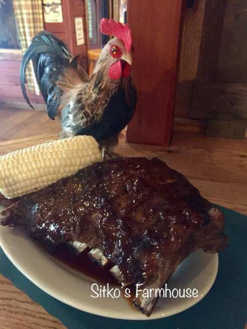 A plate of glazed ribs with corn on the cob, accompanied by a decorative rooster figurine.