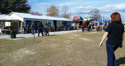 A bustling outdoor market with vendors, shoppers, and colorful flags under a blue sky.