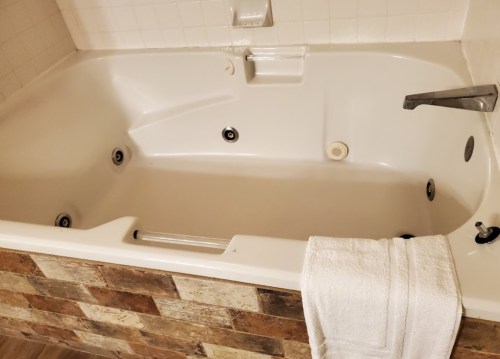 A clean, empty bathtub with jets, featuring a towel draped over the edge and a rustic stone wall.