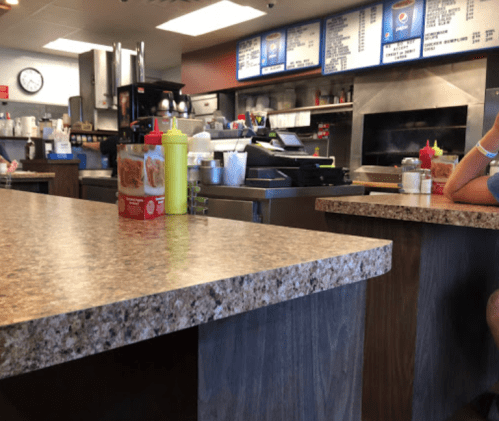 A casual diner interior with a counter, condiments, and a visible kitchen area in the background.