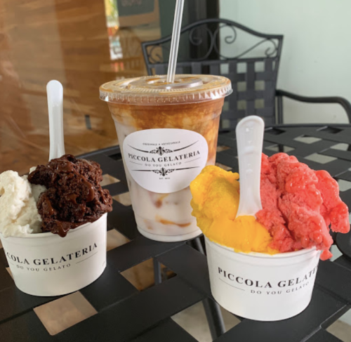 Three cups of gelato in various flavors, with a coffee drink in a clear cup, all on a black table.