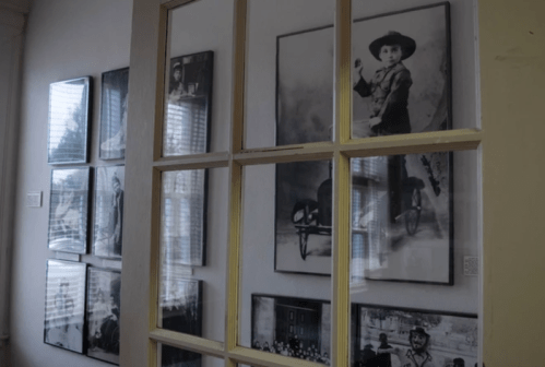 A wall displaying black-and-white photographs behind a window frame, showcasing historical images and portraits.