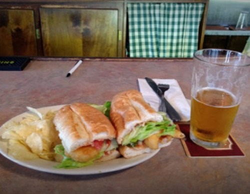 A plate with two sandwiches filled with lettuce and tomato, served with chips and a glass of beer on the side.