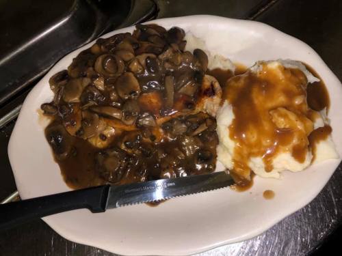 A plate of mashed potatoes and grilled meat topped with mushroom gravy, accompanied by a knife.