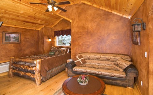 Cozy cabin interior featuring a wooden bed, sofa, and rustic decor with warm, earthy tones.